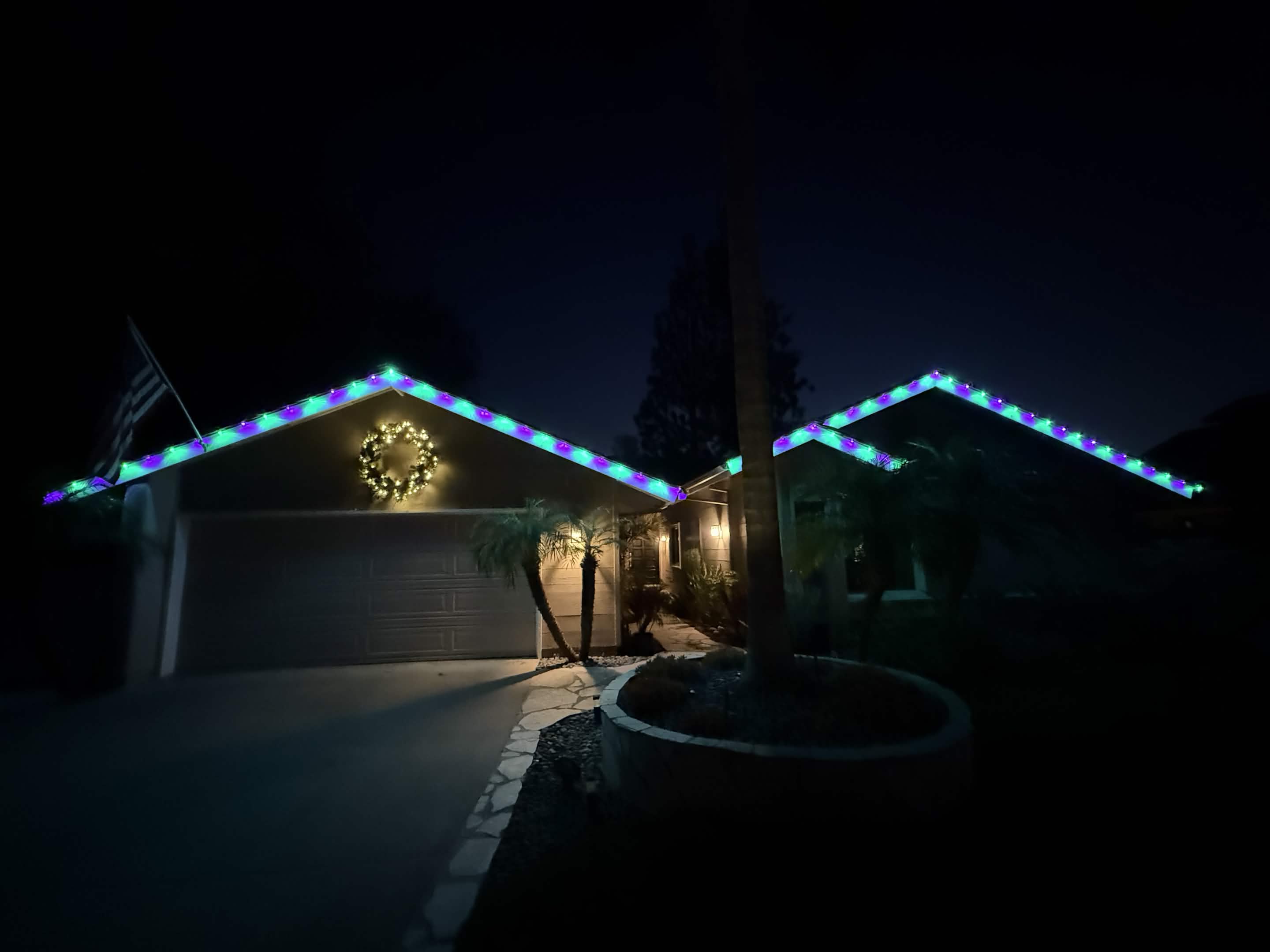 Teal and purple C9 roofline lighting with a lit wreath on a ranch home